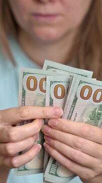 Closeup of a woman's hands counting a large sum of one-hundred-dollar bills, representing concepts like wealth, income, savings, successful business transactions, and financial planning