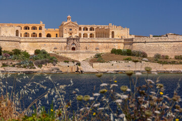 Fototapeta premium Fort Manoel on Manoel Island in Marsamxett Harbour, Malta, with limestone fortifications and waterfront view under clear blue sky.