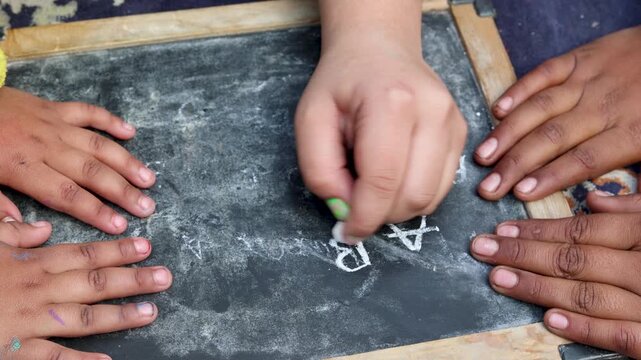 Close-up of Indian village children hands drawing with chalk on a slate board. A candid rural education moment showing creativity, learning, and traditional study methods in a simple environment.