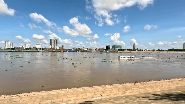 November view of tourist boat sailing upstream on Tonle Sap and Mekong river in Phnom Penh, Cambodia, with floating trees and silty water.
