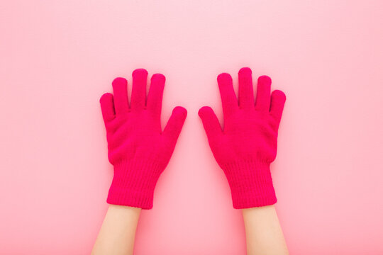 Little child girl hands in pink warm gloves on light pink table background. Pastel color. Closeup. Point of view shot. Top down view.