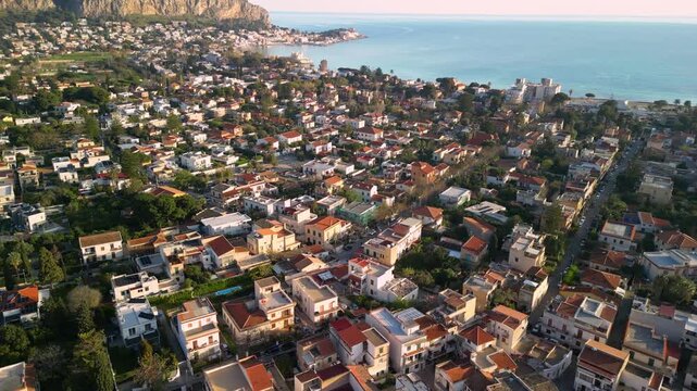 Aerial view of coastal town in Sicily, Italy, showcasing vibrant residential areas, lush greenery, and the stunning Mediterranean Sea under a clear blue sky