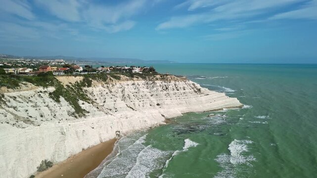 Aerial view of the stunning white cliffs along the coastline, showcasing the turquoise waves crashing against the sandy beach and lush green vegetation in the background