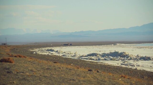 Dry Shoreline With Mountain Views. Industrial Coast Featuring Salt Piles And Rugged Peaks. Landscape Of Salt Accumulation Along Dry Shoreline With Rugged Mountain Scenery In Background