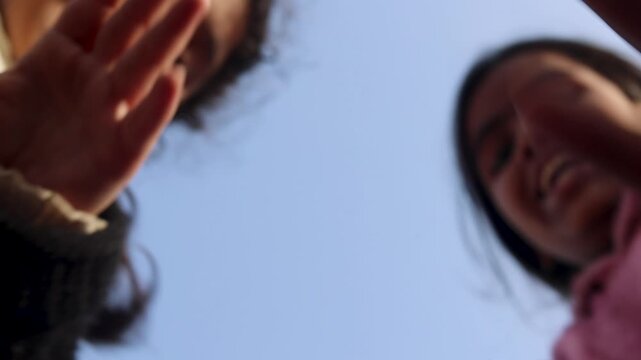 Two young Indian girls reach their hands toward the camera from a low angle, creating a playful and interactive perspective while enjoying a joyful childhood moment in a rural village setting