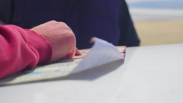 Caucasian Travelers Pointing Map On Car, Hands Flipping Paper Map With Beach And Horizon In Background, Relaxed Seaside Atmosphere, Windblown Sleeve And Casual Jacket, Collaborative Route Planning