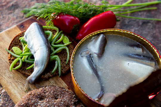 Open tin of Swedish surstromming fermented herring, traditional sandwich with rye bread, dill and peppers on rustic board, extreme food concept