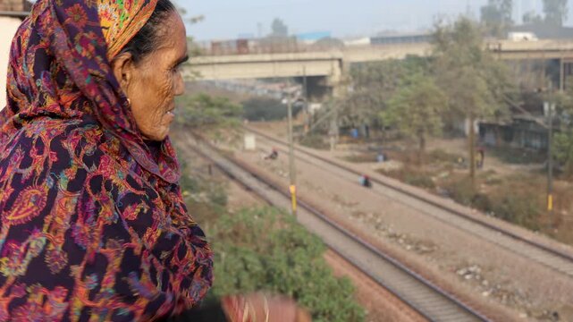 Thoughtful elderly Indian village woman gazing into distance near railway track, reflecting emotions, solitude, rural life challenges, and peaceful surroundings in Uttarakhand mountain region.