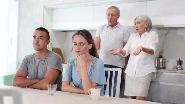 Portrait of an offended married couple in a home kitchen, which mature family members reprimand. Family conflict