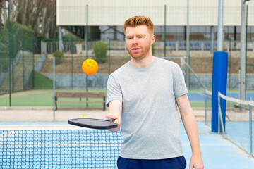 Man playing pickleball on outdoor court with orange ball © luisrojasstock