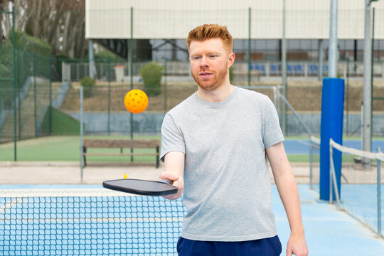 Man playing pickleball on outdoor court with orange ball