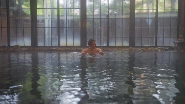Man relaxing in indoor onsen pool with large windows