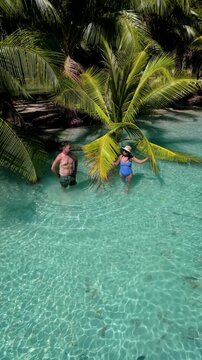 Discover the stunning beauty of Koh Kood Thailand, where two people enjoy the refreshing, clear waters surrounded by lush palm trees. A perfect escape for relaxation and fun.