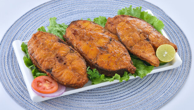 Crispy fried fish served on fresh lettuce with lemon and salad. A traditional South Asian seafood dish on a blue mat