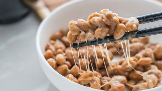  Hand using chopsticks to pick ing up the natto from the plate. Traditional Japanese food.