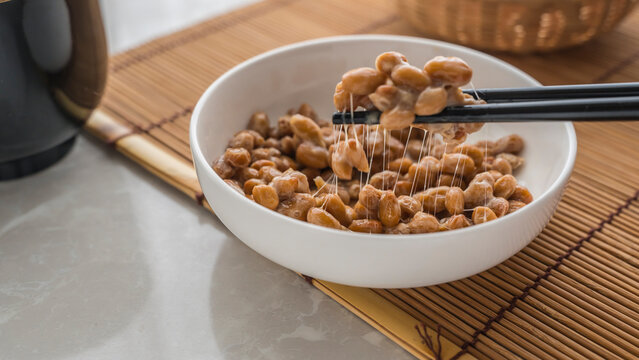 Traditional Japanese food. Hand using chopsticks to pick ing up the natto from the plate.