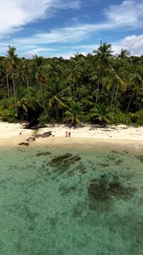 A couple explore the serene beauty of Koh Kood Island in Thailand. Relax on soft sandy beaches as gentle waves lap against the shore, surrounded by vibrant greenery and swaying palm trees.