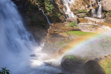 Majestic Mae Ya Waterfall in Chiang Mai, Thailand, cascades over rocks, creating a serene long-exposure effect. A vibrant rainbow arches through the mist, highlighting the natural splendor. © BestTravelPhotos