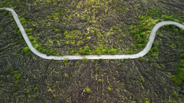 Serpentine road winds through lush greenery on solidified lava landscape, showcasing a continuous journey across a volcanic terrain with vibrant vegetation