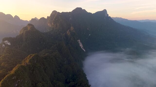 Witness the breathtaking view of Khao Sok National Park at sunrise. Gentle morning light caresses the peaks, while mist blankets the lush landscape, creating a serene atmosphere of natures beauty.