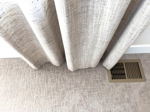 Floor vent beside curtains on light carpet