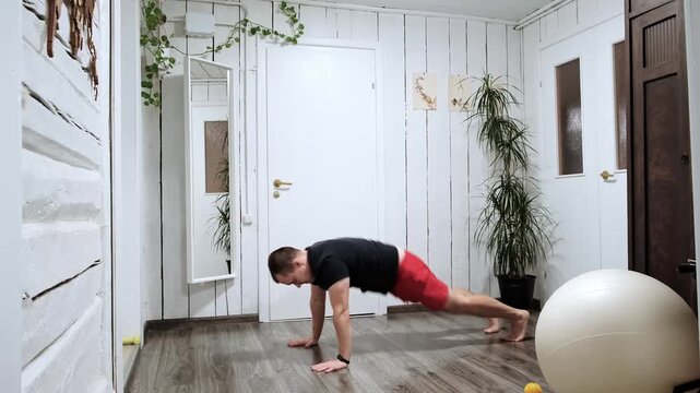 Caucasian man performs burpee exercise at home. Sporty person. Healthy lifestyle. Daily morning routine. Complex exercise including jump, squat and plank. Development of all muscle groups. 4k footage.