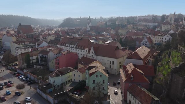 Bird's-eye view of the medieval old town of Meissen. The image shows the dense network of red tiled roofs, historical buildings, and winding alleys in warm daylight.