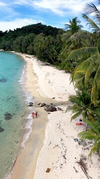Experience the beauty of Koh Kood Island in Thailand with its soft sandy beaches and crystal-clear waters. Relax under the tropical palm trees. A couple of men and women on vacation walk at the beach