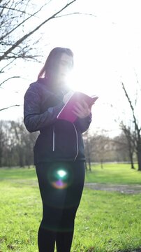 Vertical screen woman reads notes in notebook after run reviewing fitness progress outdoor workout reflection tracking results and planning next training goals healthy lifestyle routine