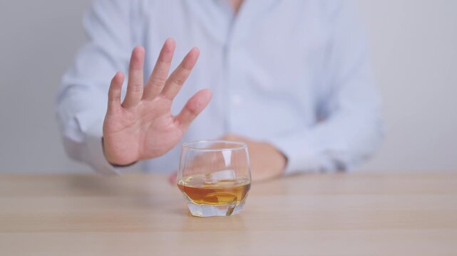 Man making stop hand gesture to refuse a glass of Cognac, Healthy man say no to alcohol drink, stop alcoholism and addiction concept. Responsible man reject a drink before driving and quit booze