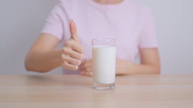 Healthy woman with glass of fresh milk and show thumbs up at home, female drinking for calcium and strong bones, high protein, dairy product for healthy lifestyle, wellness and daily routine concept