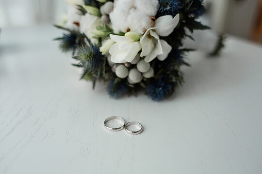 Silver wedding rings on white table with bridal bouquet of cotton eustoma and freesia.
