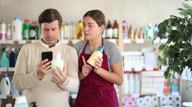 Male client, in presence of girl seller, scans barcode on product label and gives advice on applying for discount on liquid hand soap