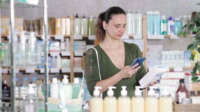 Near display case in pharmacy, woman scans barcode on atopic cream. Client collects customer information online, seek reviews and recommendations for use 