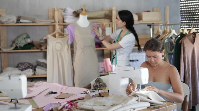Team of dressmakers works on ordering clothes from a sewing workshop. Fashion designer checks the dress sample on a mannequin, and the seamstress works at the machine. High quality 4k footage