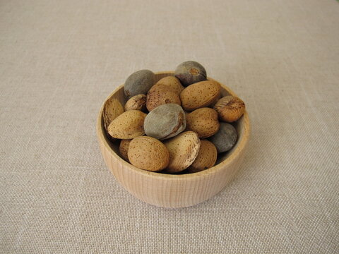 Freshly harvested almonds in a small wooden bowl, some still with their grey‑green fruit hull