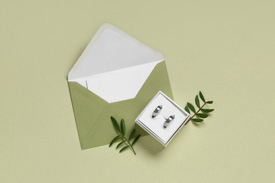 Box of wedding rings with envelope and plant branches on green background