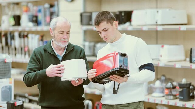 Two men of different ages choose a toaster for a kitchen. Guy helps his grandfather with the purchase of an electric toaster for bread in the household appliances. High quality 4k footage