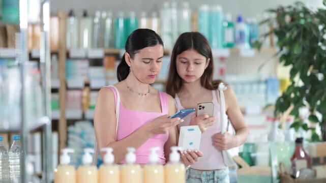 Portrait of attentive mother and daughter choosing box with pills to improve well-being in pharmacy, scan QR code on label