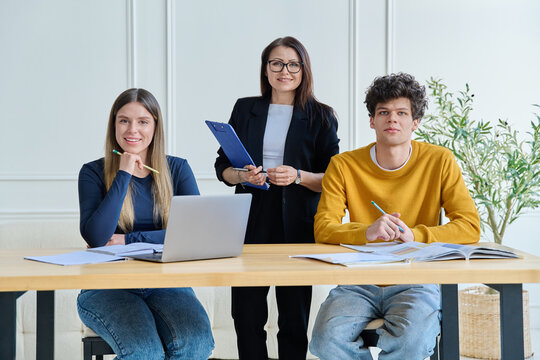 Two university students with female teacher mentor study while sitting at desk