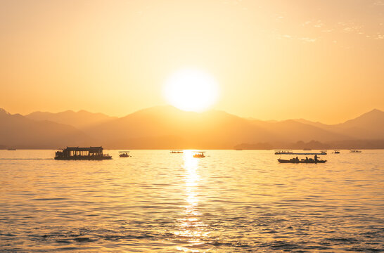 Golden sunset over West Lake with traditional boats carrying passengers in Hangzhou, China