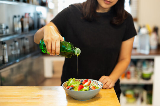 Woman pouring olive oil from bottle onto a fresh salad with lettuce strawberries and blueberries in a kitchen.