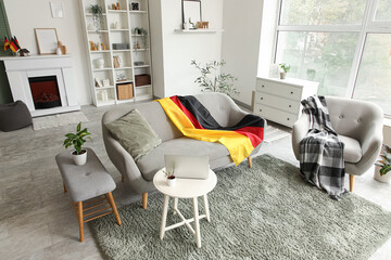 Obraz premium Interior of light living room with German flag on sofa and armchair