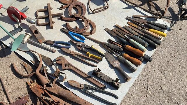 Vintage tools spread on blanket sunlit flea market display of rusty pliers wrenches horseshoes bolts and hand tools collector.