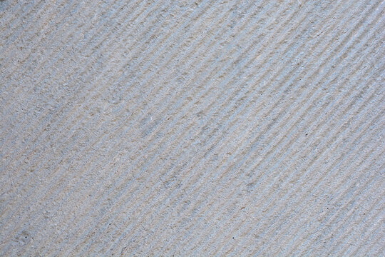 A close up of a gray stone surface with fine diagonal chiseled lines and a rough granular texture
