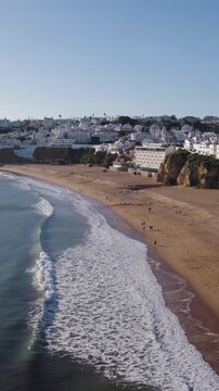 Vertical aerial pushback shot moving away from Albufeira beach, a famous sandy coastline in Algarve, Portugal.