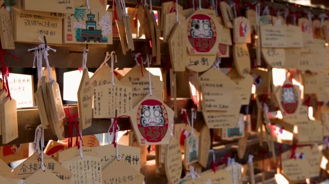 A close up slow motion shot of wooden prayer tablets or ema at a shinto shrine in japan hanging and swaying in the breeze.