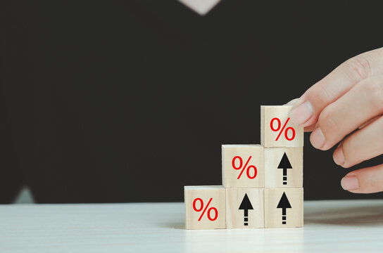 Rising financial interest rate graph concept. Businessman arranges wooden blocks with increasing percentage arrow icons, financial business, investing or home mortgages, inflation.
