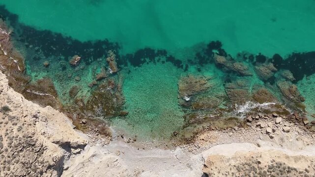 Descending drone top down over rocky Mediterranean beach and seabed