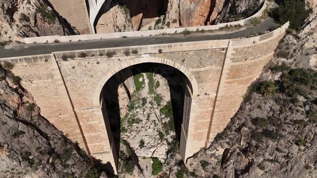 Ascending drone shot revealing first bridge arch in Mascarat Canyon with traffic